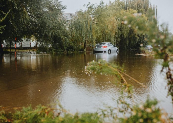A car struggles through a flooded street surrounded by trees after a heavy rainstorm.