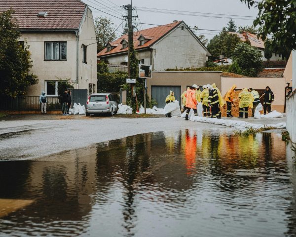 Emergency workers in rain gear manage floodwaters in a suburban street.